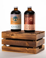 Two bottles of Life Itself mushroom products resting on a rustic wooden crate against a white background, featuring Wild Harvested Chaga Concentrate and Chaga Birch Beer Syrup.